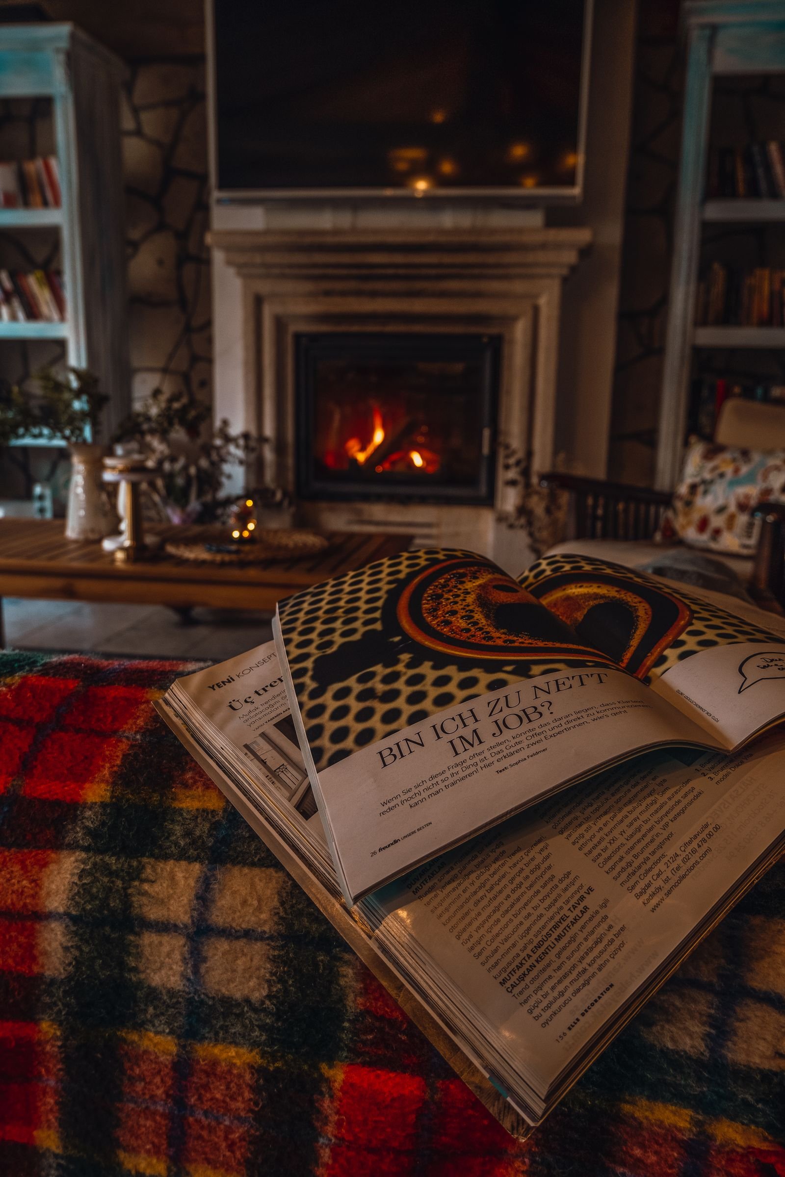 A warm living room lit by a fireplace with an open magazine on a low table